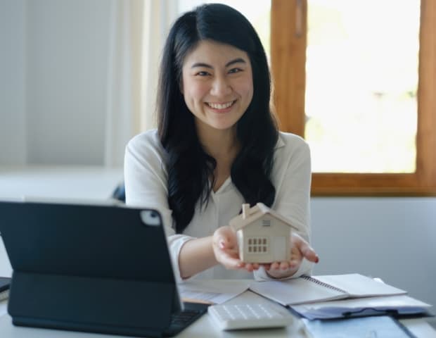 Lady in a messy office holding a small model house