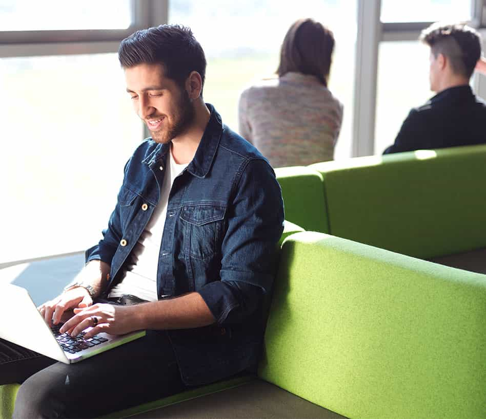 Hip guy sitting on a bright green airport lounge working on his laptop